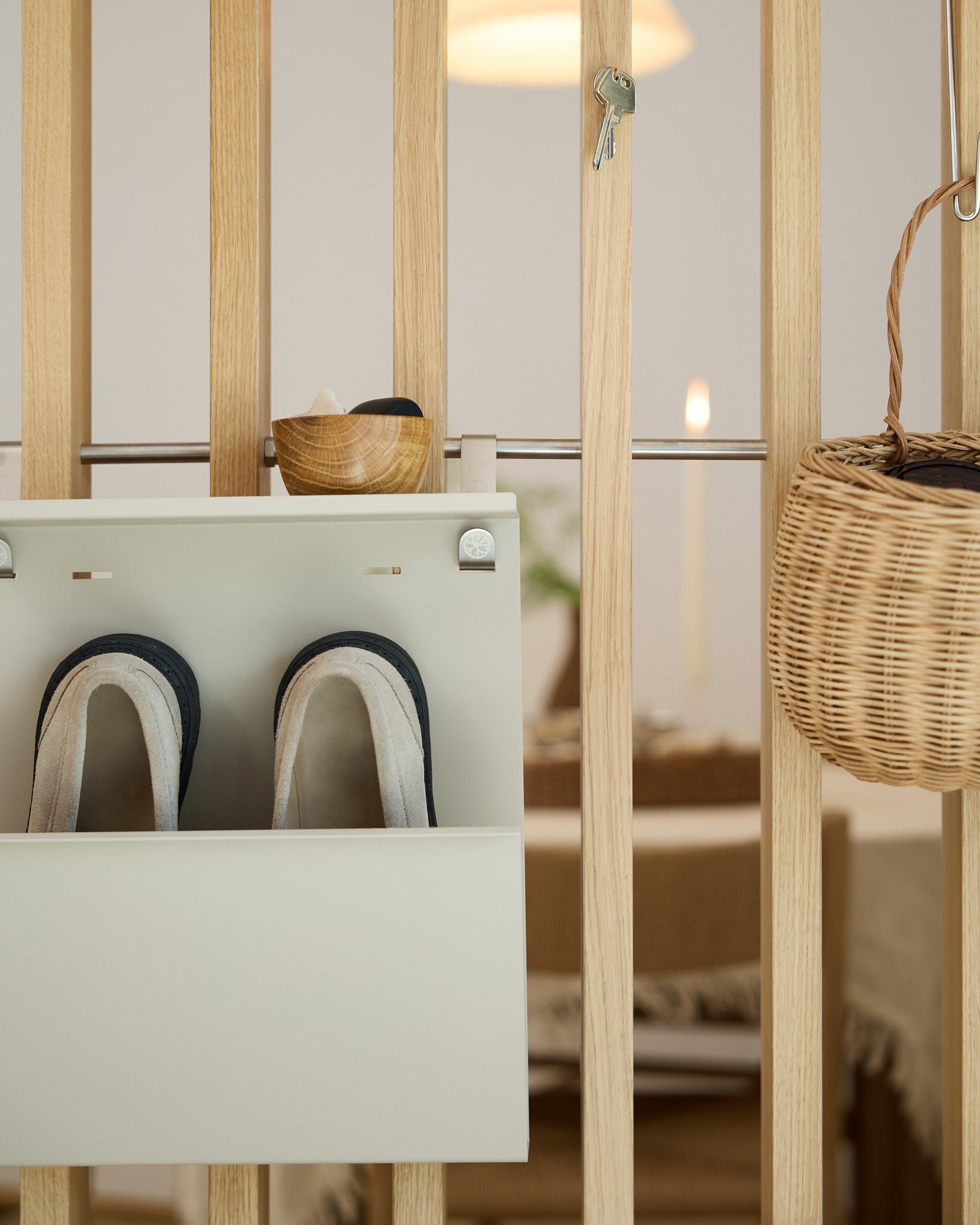 WoodUpp Nell Beige Shoe Storage eksponuje kapcie, miskę i wiklinowy kosz na drewnianej ściance działowej; w tle widać jadalnię.