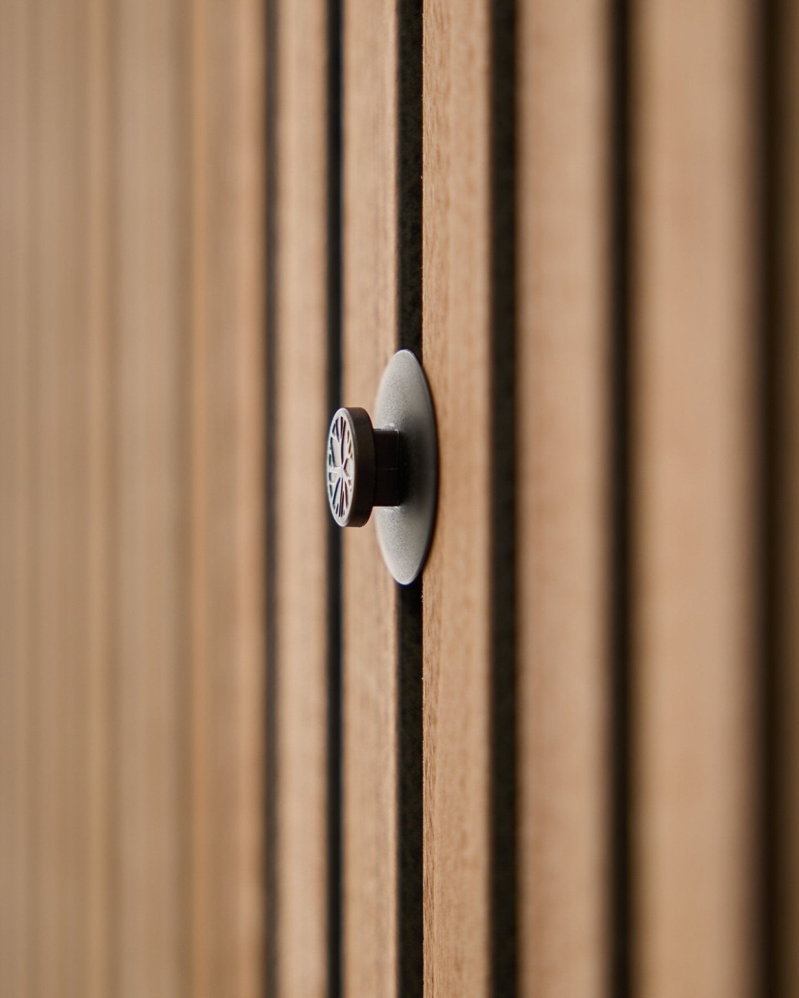 Zbliżenie na zestaw Dupps | Light knob set (3 knobs plus tool) od WoodUpp zamontowany na panelu akustycznym z lamelami, z delikatnie rozmytymi drewnianymi lamelami w tle.
