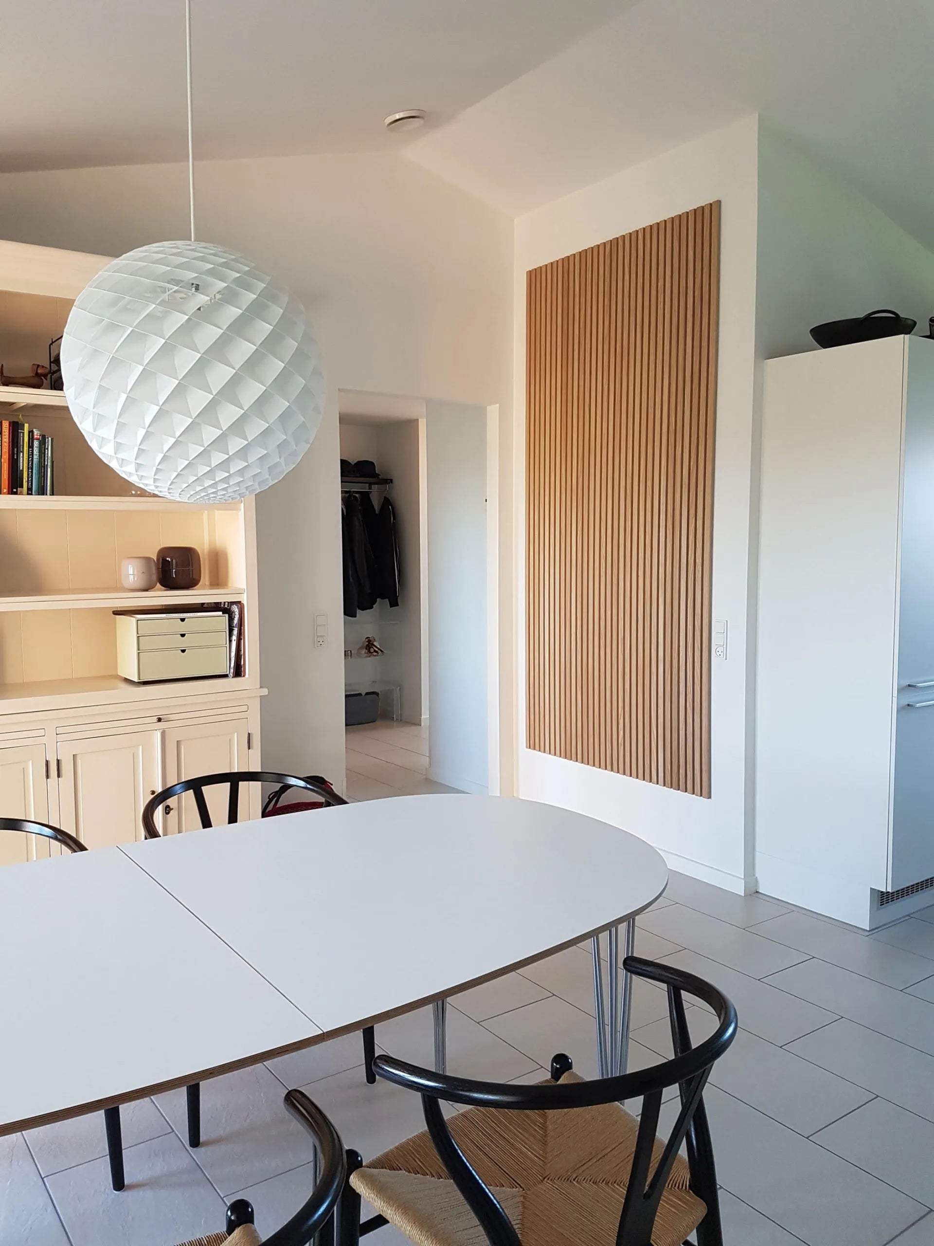 Nowoczesna jadalnia z białym owalnym stołem, czarnymi krzesłami, dużą teksturowaną lampą wiszącą i eleganckimi szafkami z jasnego drewna Akupanel.
