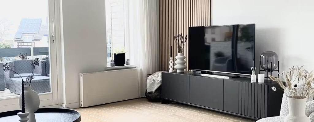Nowoczesny salon z czarną szafką pod telewizor, telewizorem z płaskim ekranem, dekoracyjnymi wazonami i dużymi oknami z naturalnym światłem wychodzącymi na patio; Akupanel na jednej ścianie.