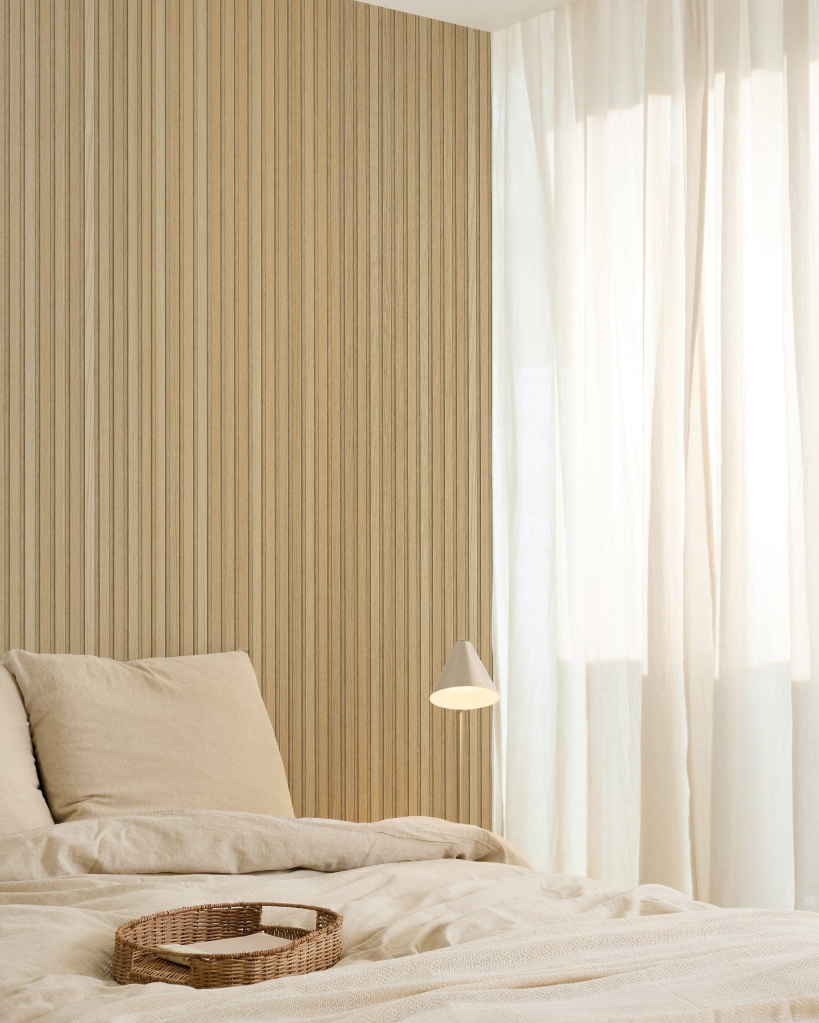Minimalistyczna sypialnia z pościelą beige, wiklinową tacą, nowoczesną lampą ścienną, akcentową ścianą z akustycznych paneli drewnianych Akupanel oraz lekkimi zasłonami rozpraszającymi miękkie naturalne światło.
