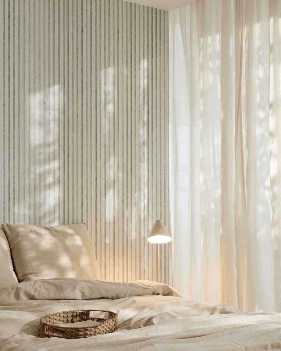 Minimalistyczna sypialnia z pościelą beige, plecioną tacą, pasiastą tapetą oraz akustycznym panelem drewnianym WoodUpp Akupanel w kolorze Snow Grey Felt do pochłaniania dźwięku.