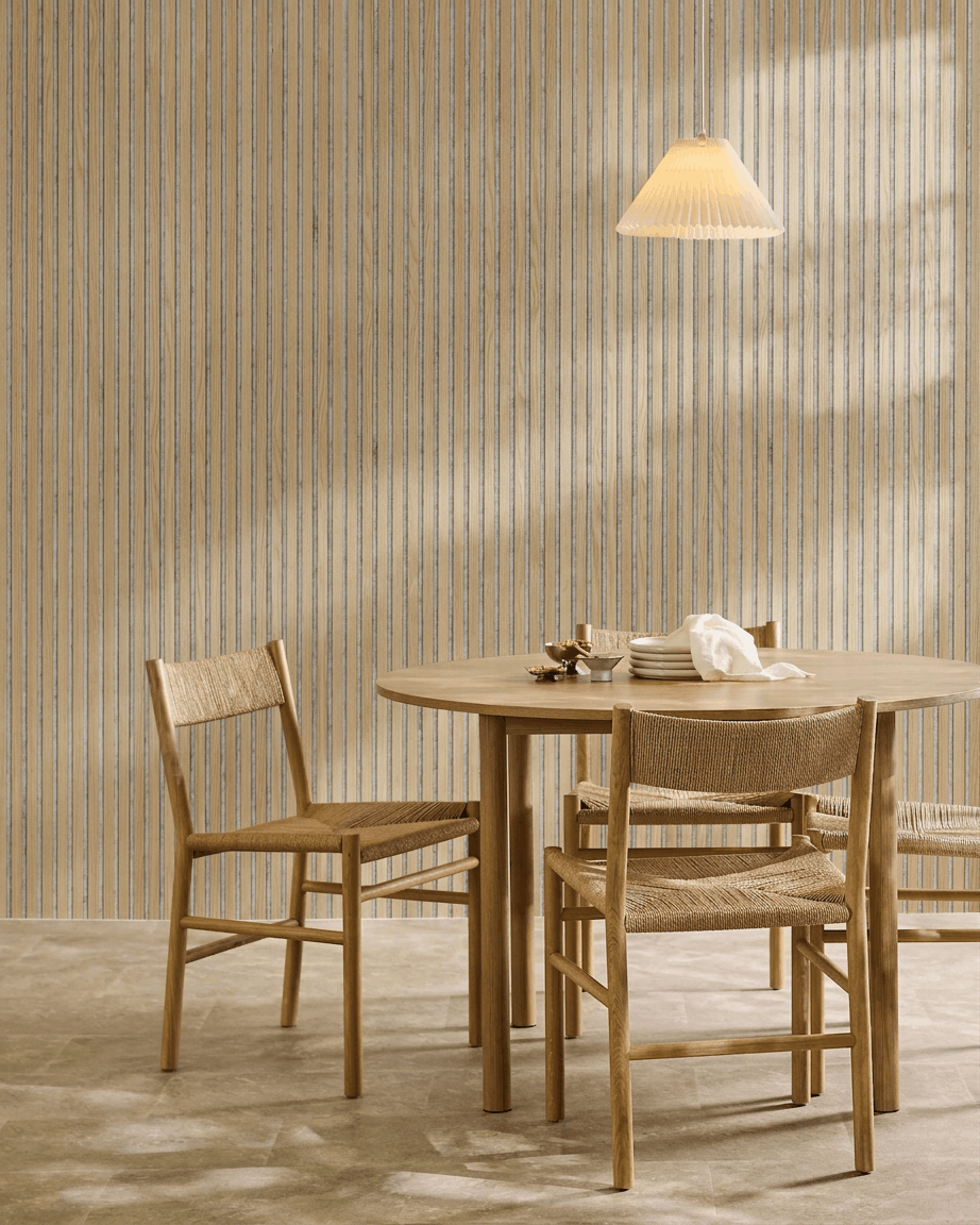 Minimalistyczna jadalnia z okrągłym drewnianym stołem, plecionymi krzesłami, lampą wiszącą i akustycznym panelem drewnianym WoodUpp Akupanel w kolorze Classic Oak z filcem grey.