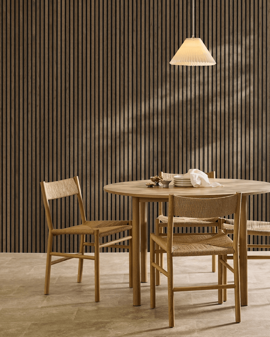 Minimalistyczna jadalnia z okrągłym stołem, plecionymi krzesłami i lampą wiszącą, z akustycznym panelem ściennym z lamelami WoodUpp Akupanel Rustic Grey Oak.