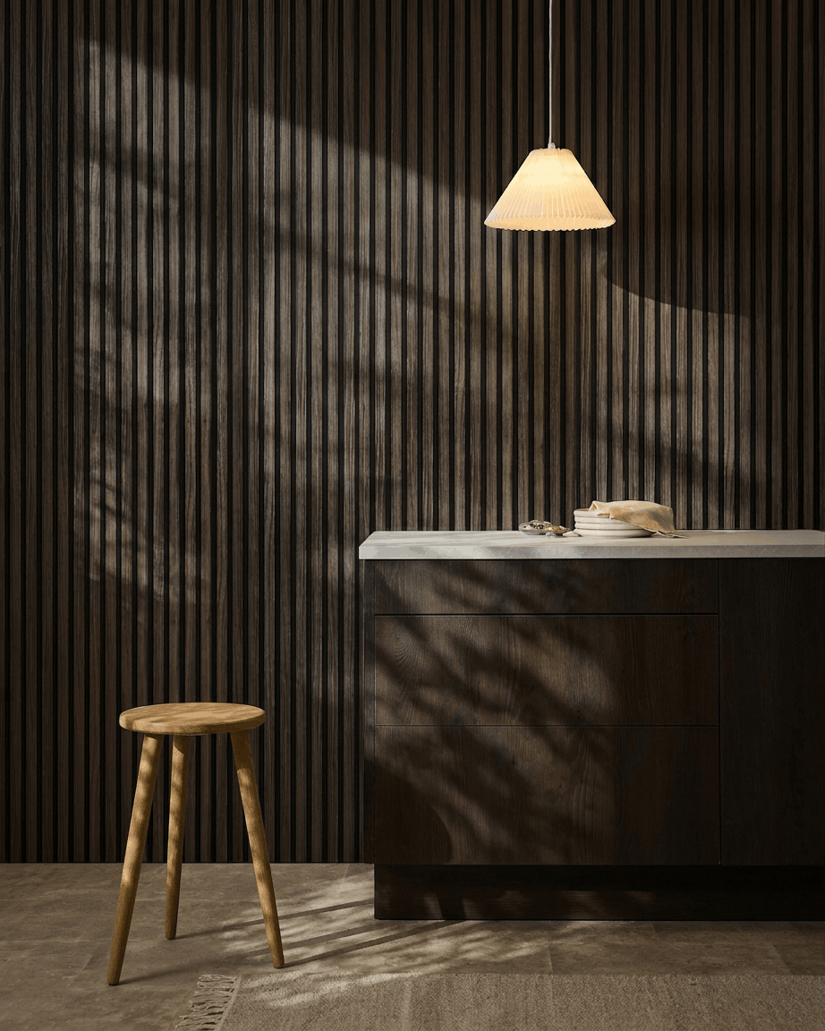 Minimalistyczna kuchnia z panelami akustycznymi WoodUpp Akupanel Black Oak na ścianie, drewnianym stołkiem, białym blatem, lampą wiszącą beige i cieniami skąpanymi w słońcu.