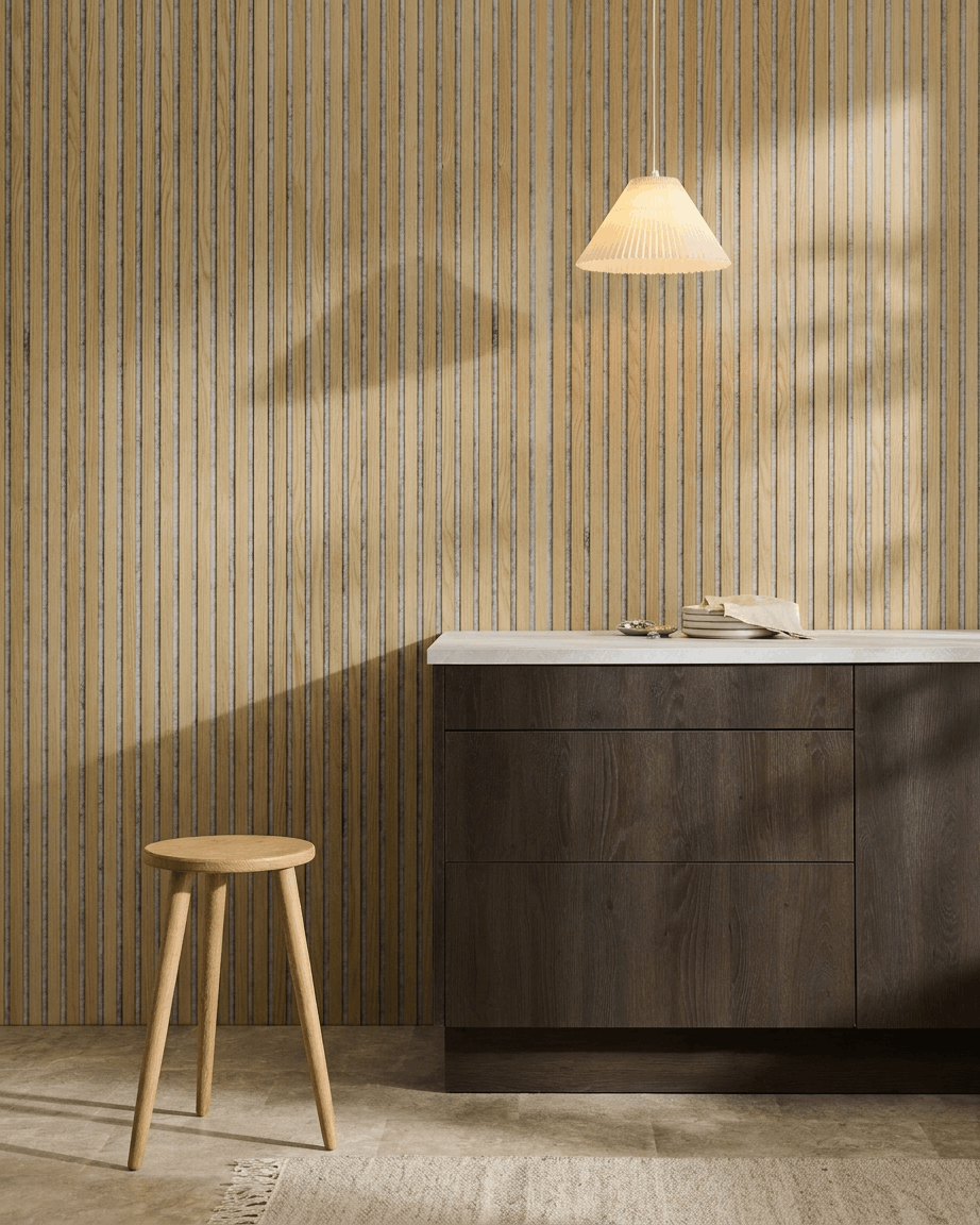 Minimalistyczne wnętrze w stylu nordyckim z panelem WoodUpp Akupanel Panel akustyczny w kolorze Classic Oak z filcem Grey, zestawionym z drewnianym stołkiem, ciemną szafką i białym blatem.