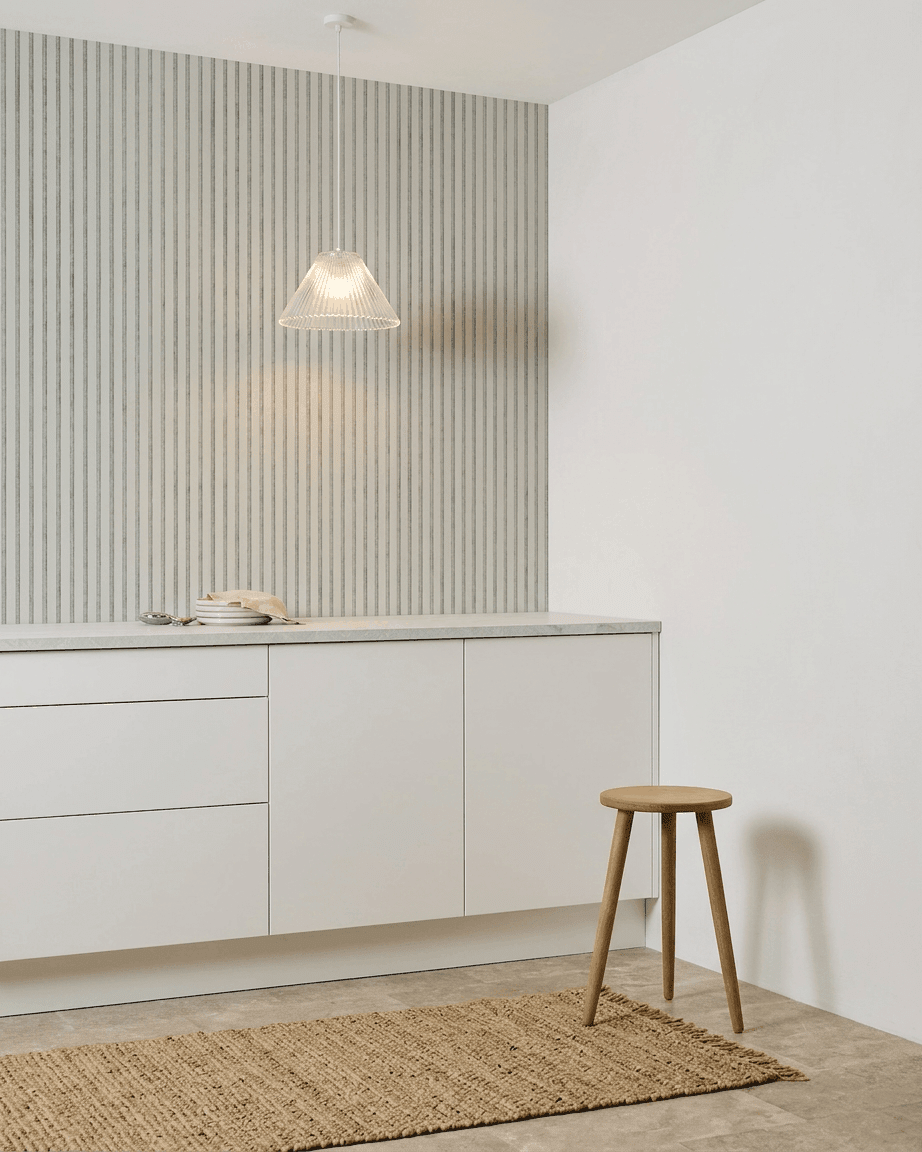Minimalistyczna kuchnia z białymi szafkami, drewnianym stołkiem, plecionym dywanem i panelem WoodUpp Akupanel Snow Panel akustyczny, zamontowanym dla pochłaniania dźwięku.