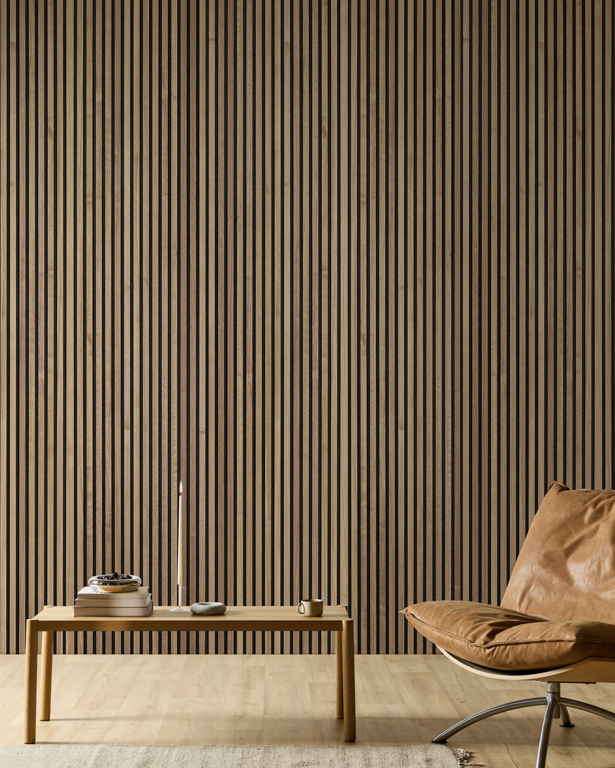 Minimalistyczne pomieszczenie z skórzanym fotelem, drewnianą ławką, książkami, świecą i nowoczesną akustyczną ścianą z drewnianych listew Akupanel jako akcentem w neutralnych tonach.