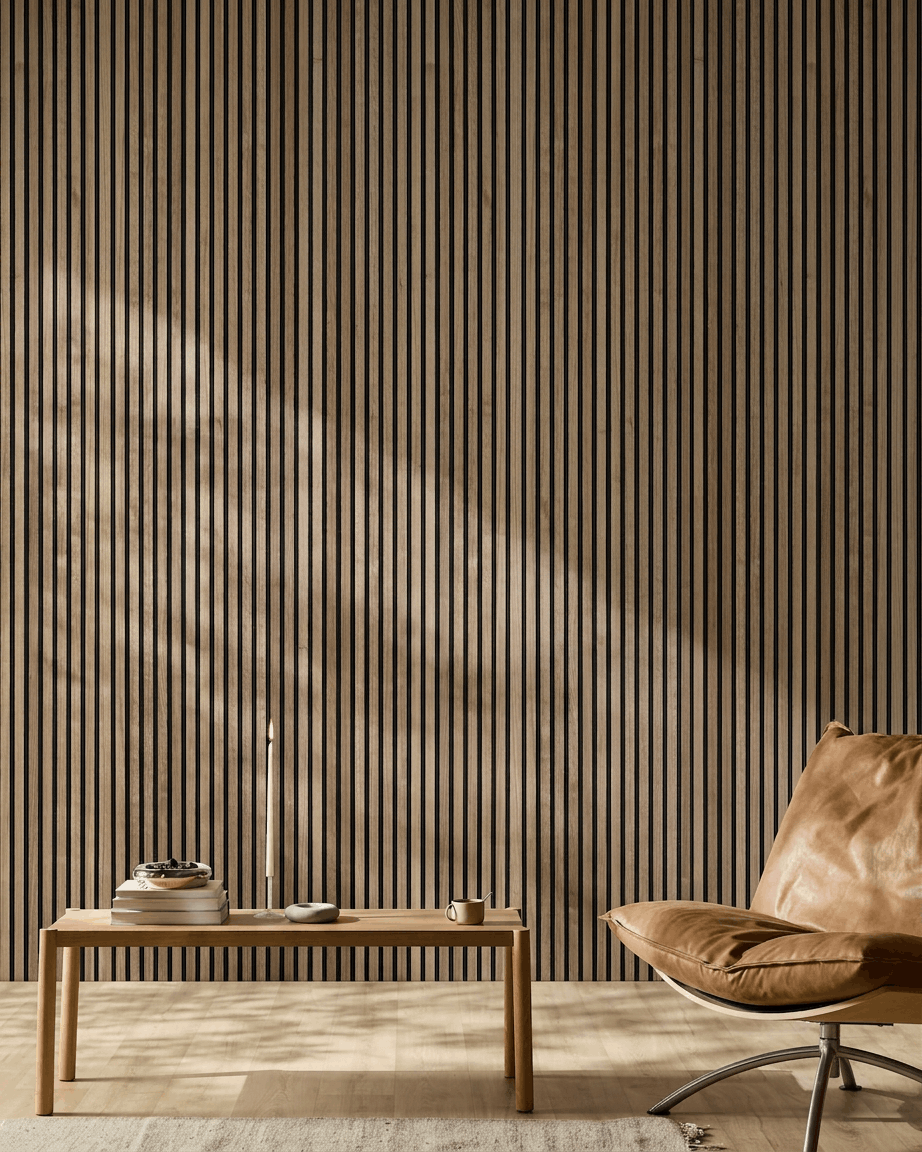 Minimalistyczne nordyckie wnętrze z akustycznym panelem drewnianym WoodUpp Akupanel w kolorze orzechowym, krzesłem z jasnobrązowej skóry i drewnianym stolikiem kawowym z książkami i świecą.