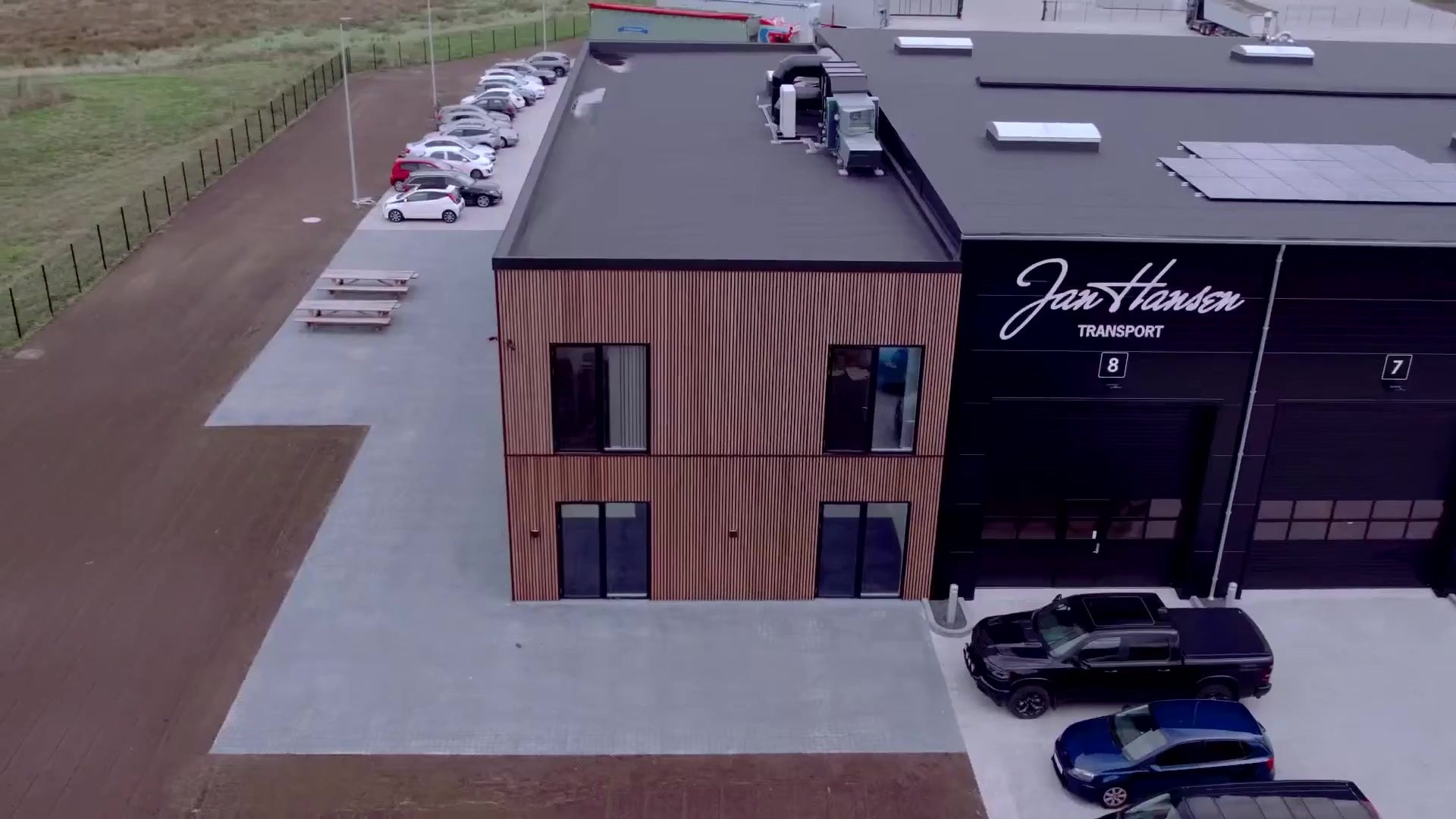 Two-storey transport company building clad in vertical brown Aluwood slats beside a black warehouse section, seen from the air