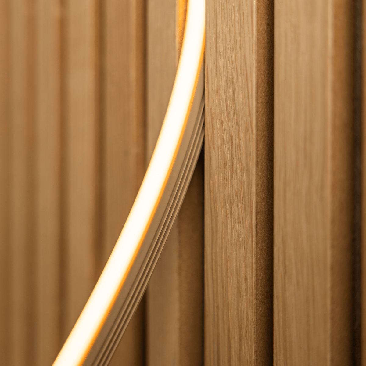 Zbliżenie na taśmę LED WoodUpp Lumi w kolorze beige (240 cm), emitującą ciepłe żółte światło na akustyczne lamele drewniane Akupanel vertical; kompatybilna z Philips Hue.