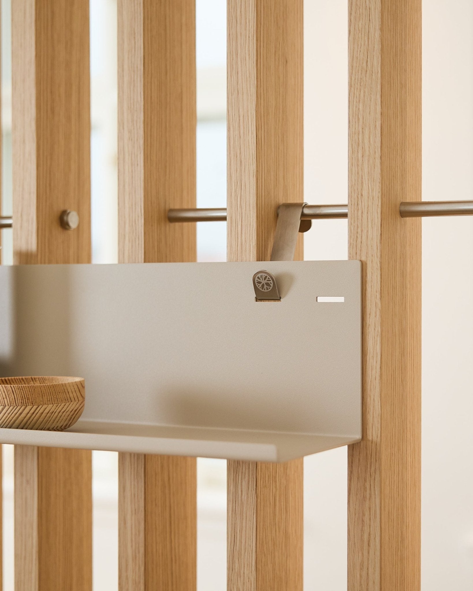 Beige metalowa półka WoodUpp BM1 (63 x 13,4 cm) zamontowana na akustycznym panelu ściennym z lamelami vertical, z drewnianą misą po lewej stronie półki.