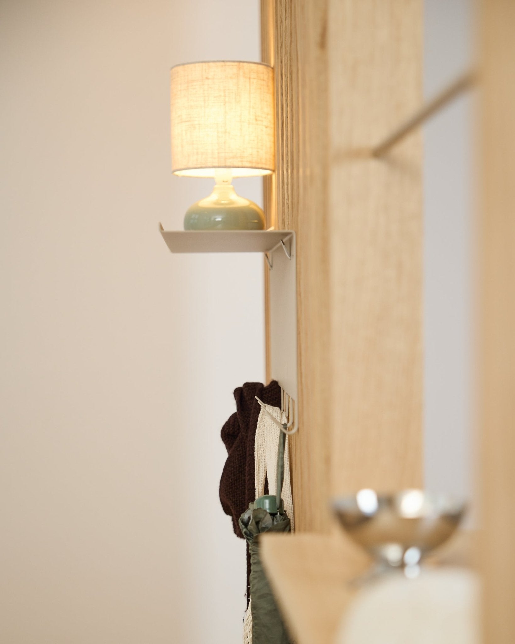 beige wieszak WoodUpp Nell BM1 (63,5 x 24 cm) stoi pod lampą stołową small, obok ściany z jasnego nordyckiego drewna Panel akustyczny.