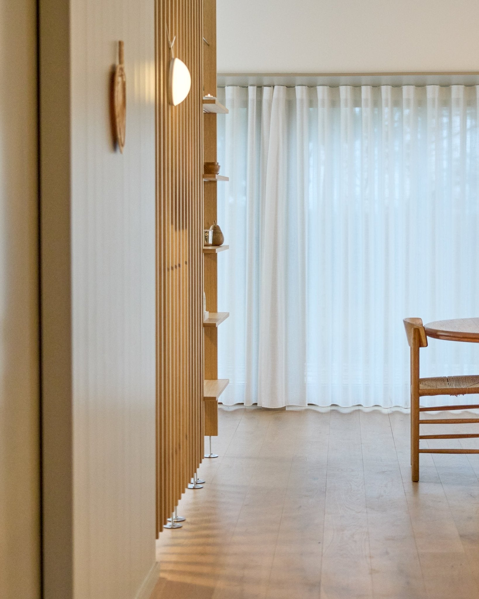 Minimalistyczne wnętrze z przegrodą pokojową WoodUpp Embrace od podłogi do sufitu, drewnianą podłogą, półkami, krzesłem i lekkimi zasłonami przy oknach large.