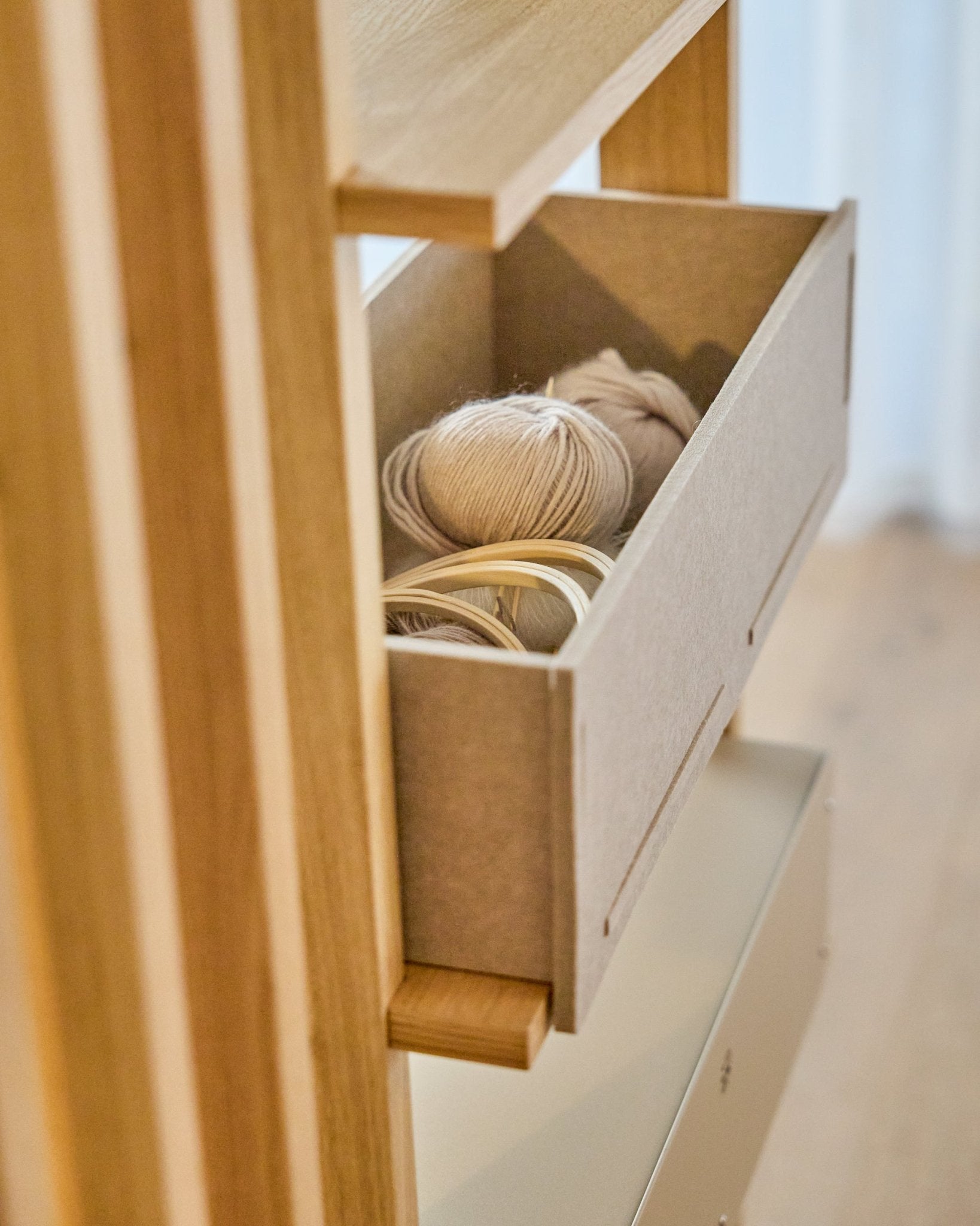 WoodUpp Vigg Felt Box / BM2 w kolorze beige mieści lekkie motki włóczki i drewniane tamborki hafciarskie na drewnianym regale, tworząc spójną całość z nordyckimi panelami akustycznymi.