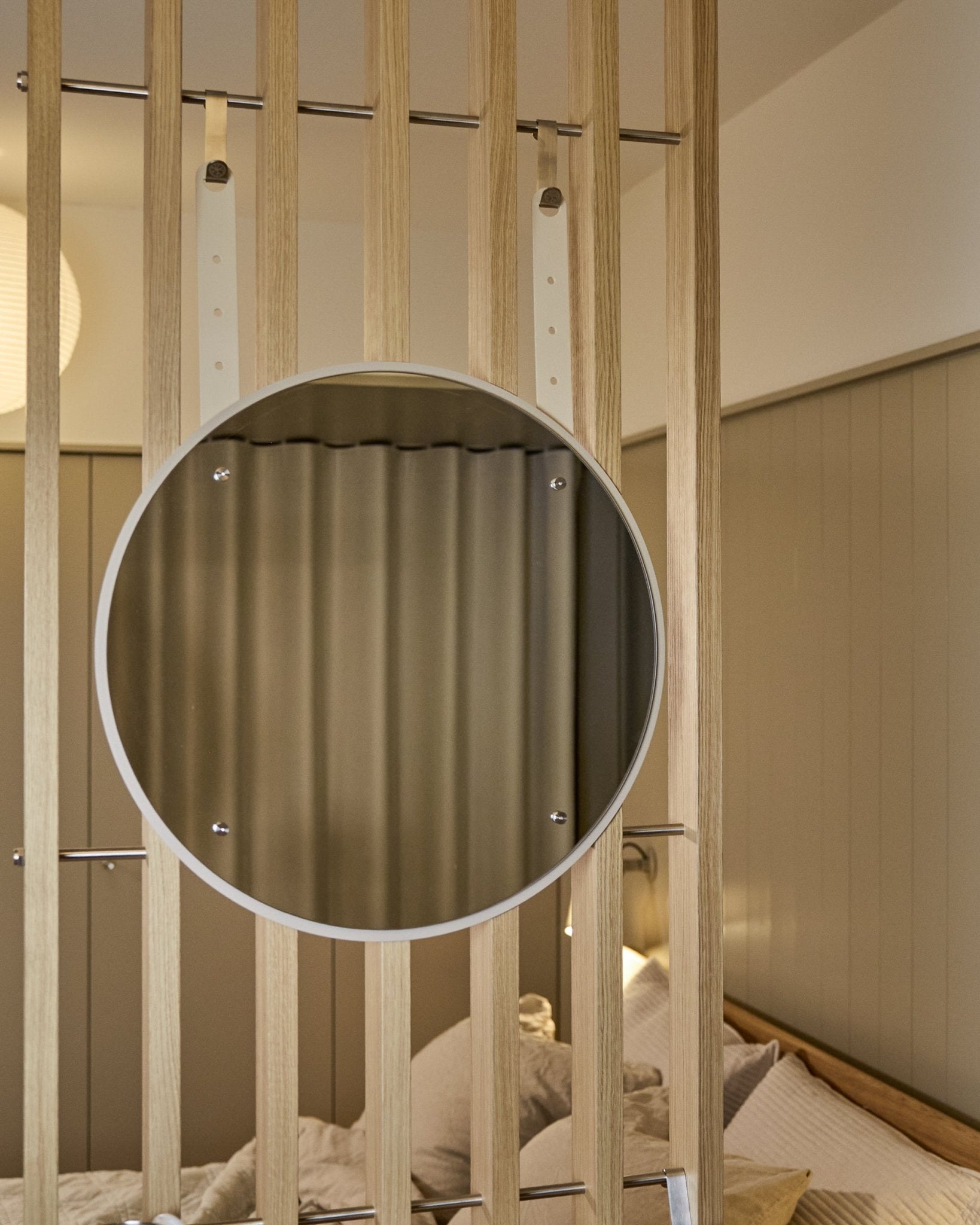 Okrągłe lustro Vala BM1 z regulacją wysokości od WoodUpp, o średnicy 54 cm, zamontowane na vertical akustycznym panelu z drewnianych lameli, w miękkim, neutralnym świetle.