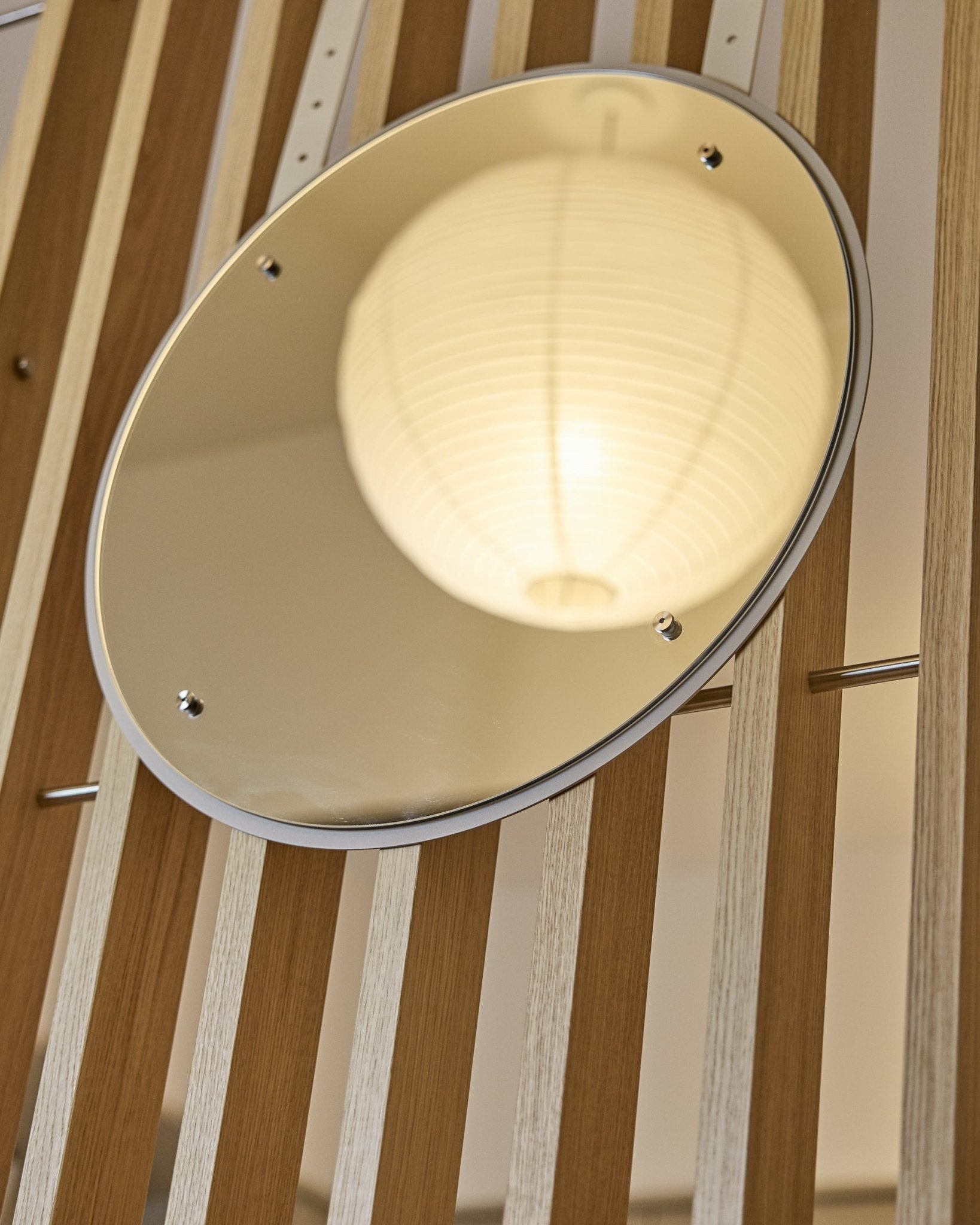 Vala | Mirror / BM1, D54 cm od WoodUpp to okrągłe lustro z regulacją wysokości, zamontowane na vertical akustycznych panelach lamelowych, w którym odbija się świecąca papierowa latarnia.
