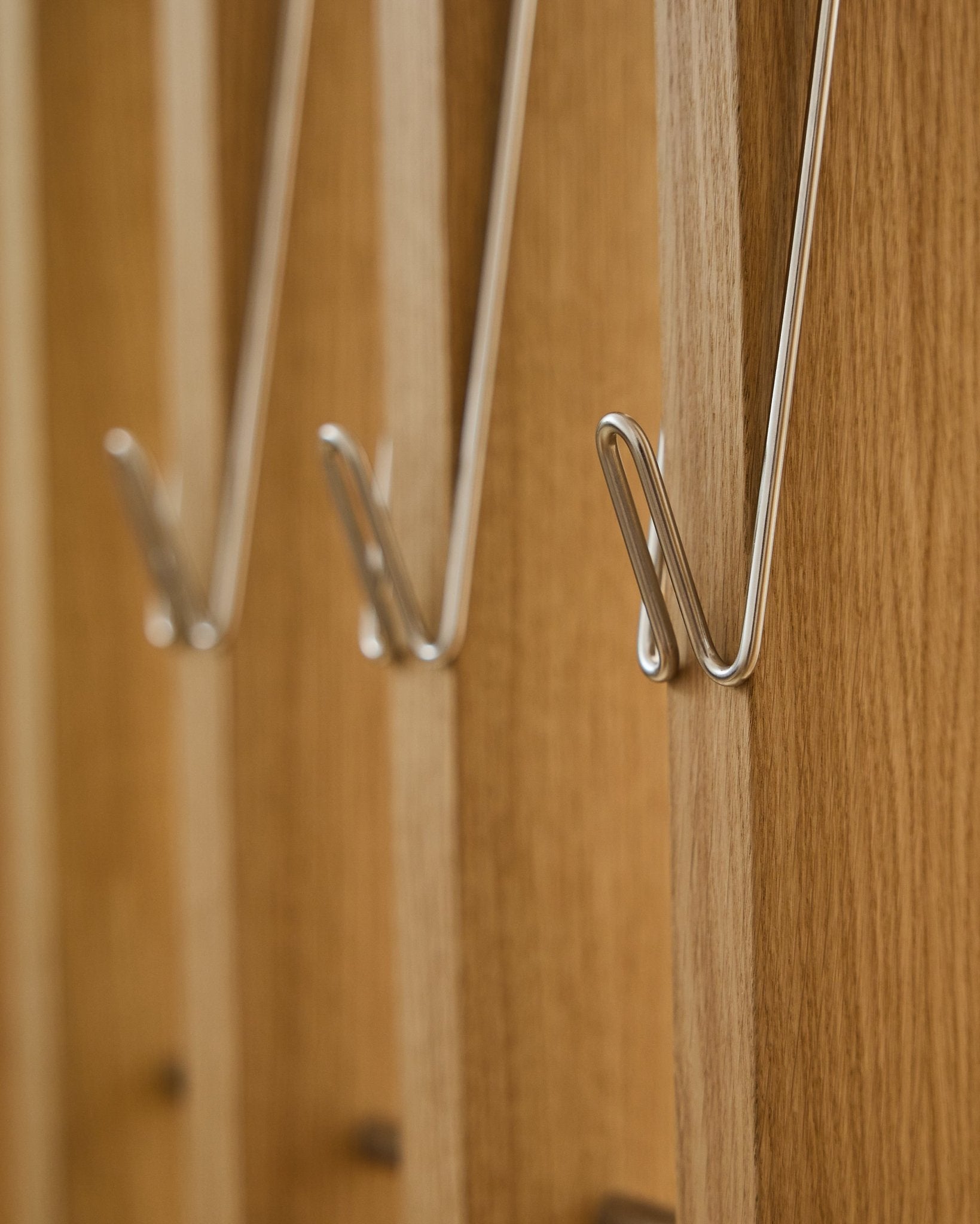 Zbliżenie na trzy Alva | Wire Hook / BM1, Stainless Steel, Long marki WoodUpp, zamontowane w rzędzie na akustycznych panelach drewnianych Akupanel i rzucające delikatne cienie.