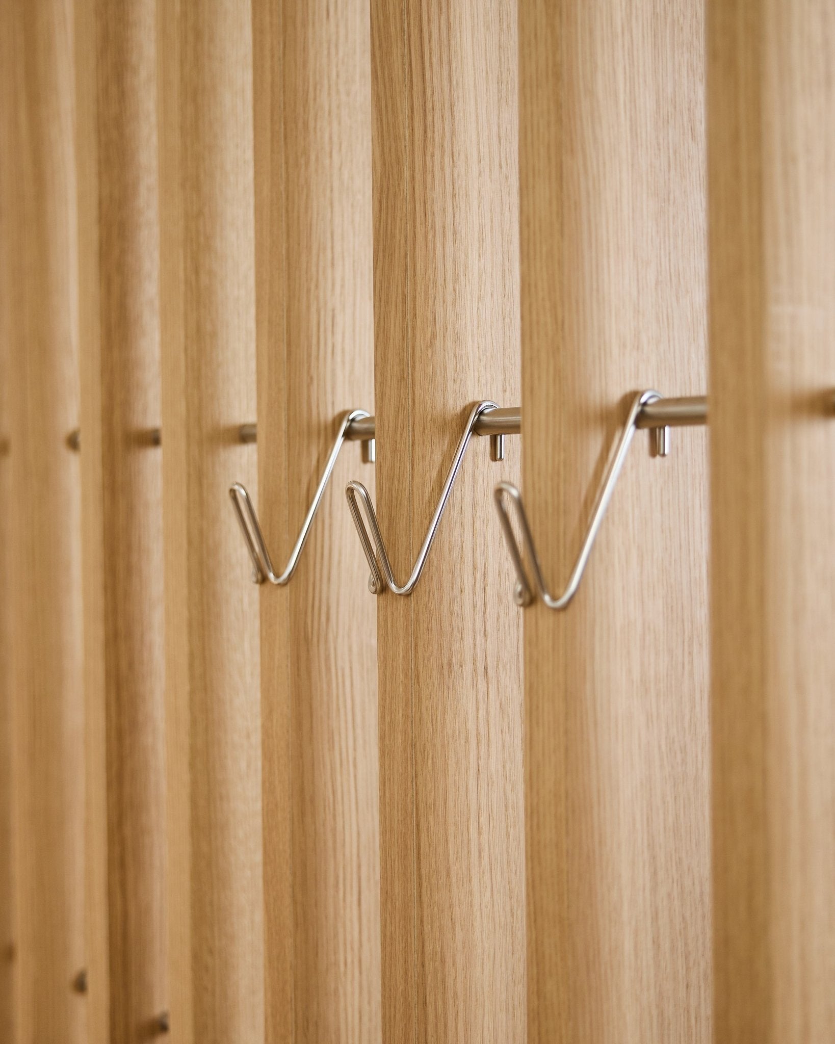 Trzy krótkie akcesoria WoodUpp Alva Wire Hook / BM1 ze stali nierdzewnej steel są zamontowane równomiernie w jednym rzędzie na akustycznym panelu z drewnianych listew vertical.
