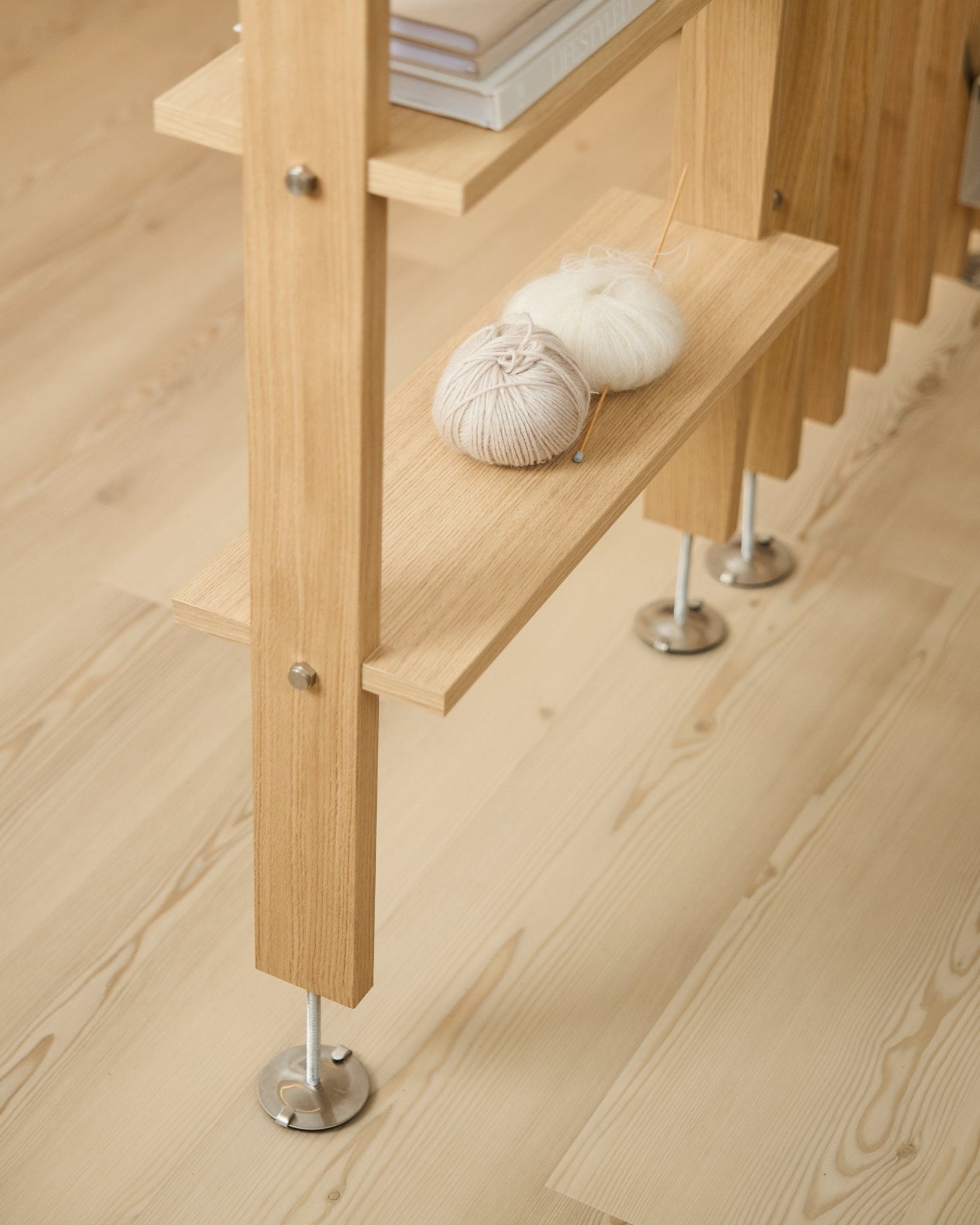 Półka Lova | Wood Shelf / BM2 od WoodUpp w fornirze dębowym (65,8 x 20 cm), z włóczką i drutami na dolnej półce, na jasnej drewnianej podłodze z metalowymi nogami.