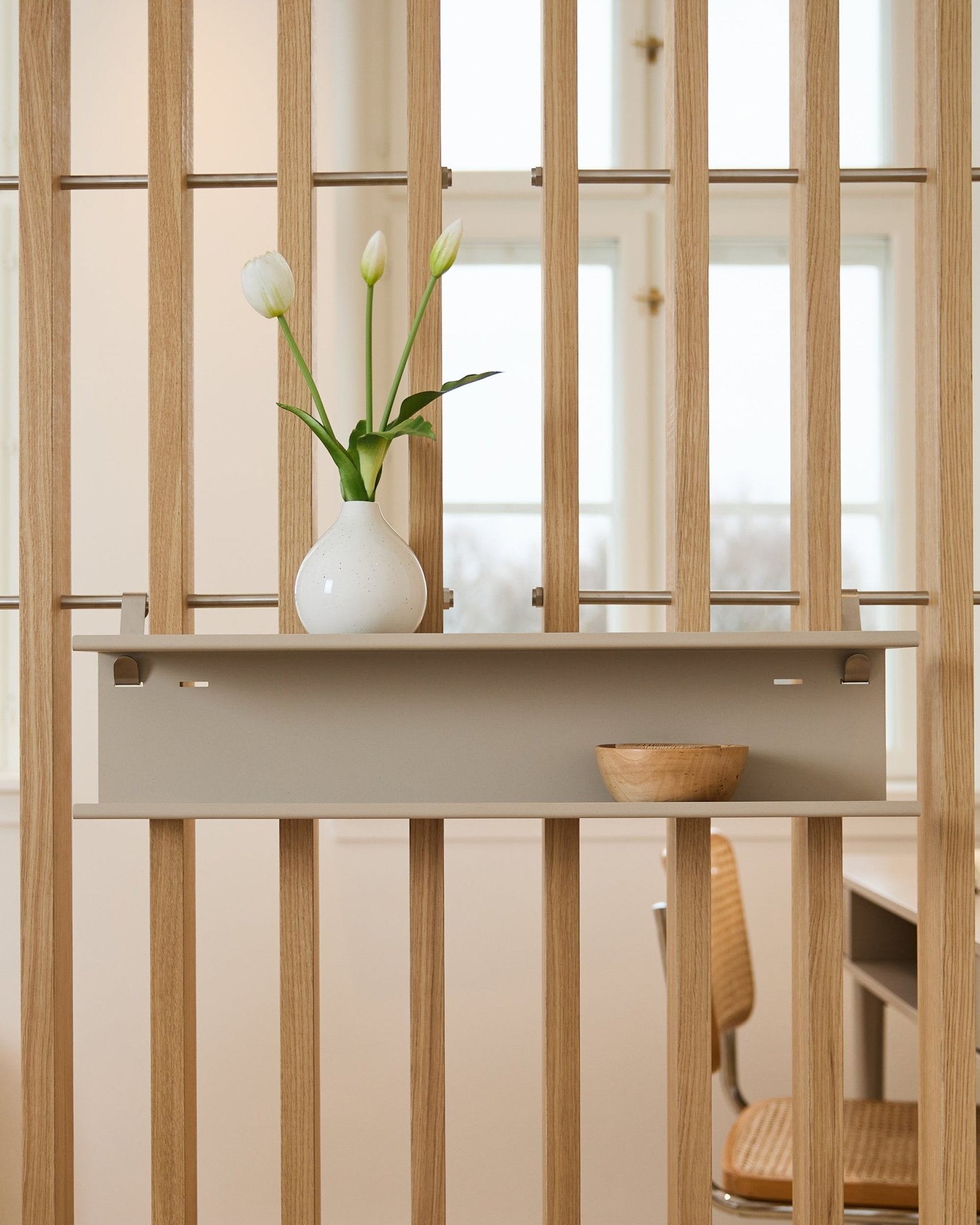 Podwójna metalowa półka / BM1 od WoodUpp w kolorze beige (63,5 cm), zamontowana na lamelowej ściance działowej, zaaranżowana z wazonem i drewnianą misą.