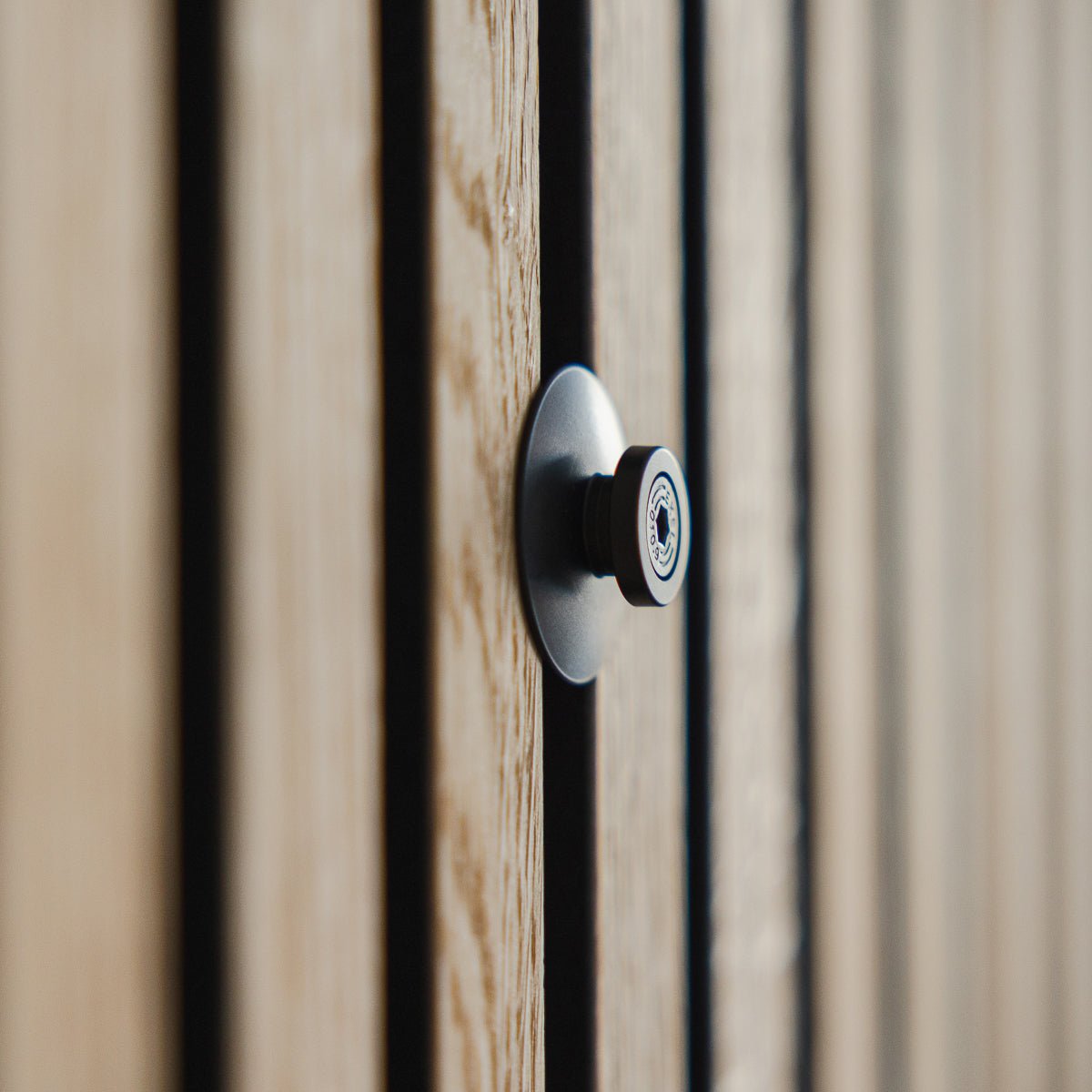 Zbliżenie na Dupps | ciężki wizjer od WoodUpp z aluminium black, zamontowany w ryflowanych drewnianych drzwiach z lamelami akustycznymi Akupanel, z ostro ustawionym obiektywem.