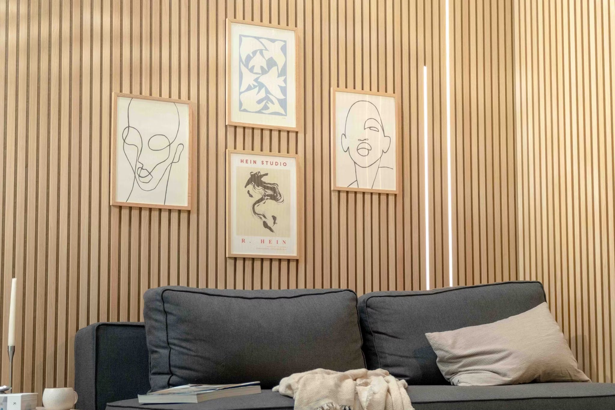 Nowoczesny salon z ciemną sofą z beżową poduszką, zaakcentowany skandynawską ścianą z drewnianych listew akustycznych Akupanel i minimalistyczną skandynawską sztuką powyżej.